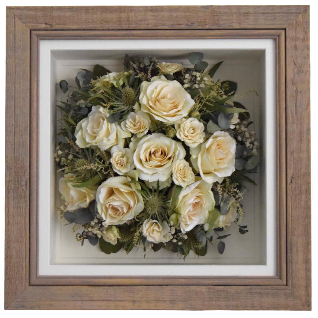 Round preserved wedding posy of white roses in a rustic wooden frame